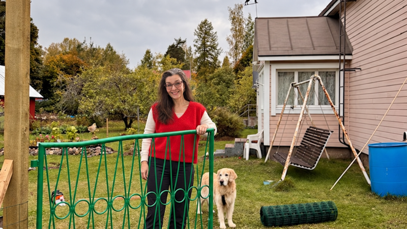 Nainen punaisessa Amélie-mohairneuleliivissä talon vihreällä portilla, kultainennoutaja Mortti vieressä